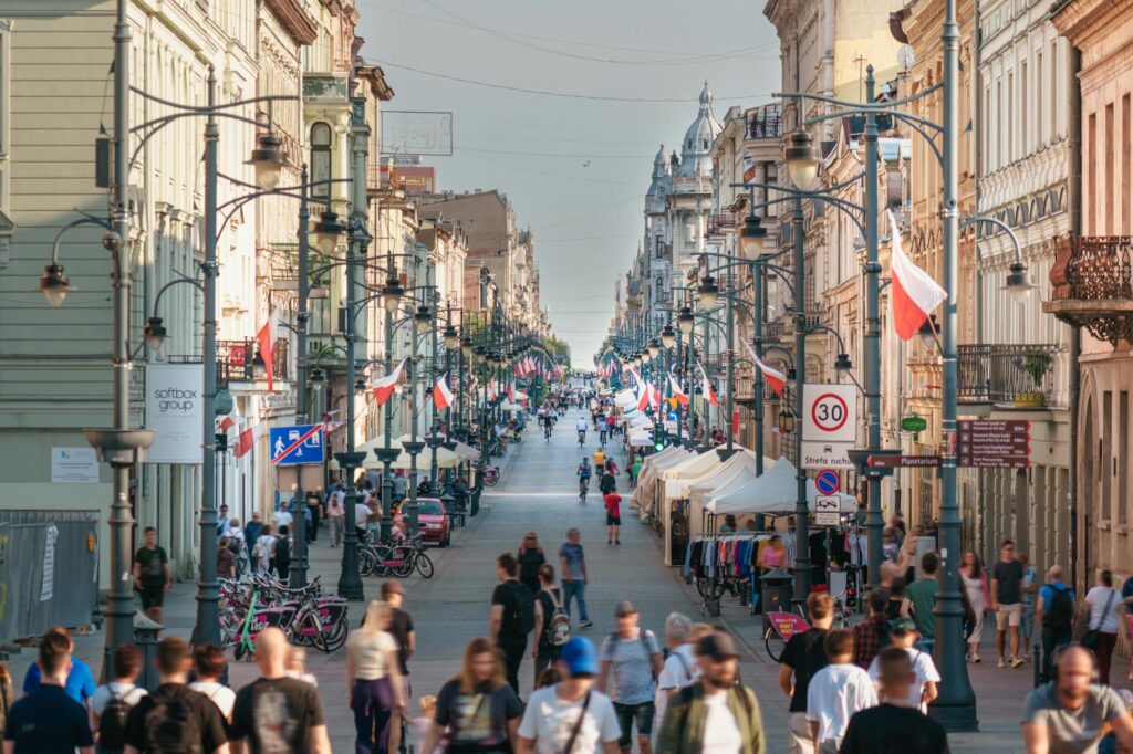 Busy scene on Piotrkowska Street, Łódź with flags and people walking. A vibrant cityscape showcasing Polish culture.