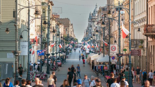 Busy scene on Piotrkowska Street, Łódź with flags and people walking. A vibrant cityscape showcasing Polish culture.