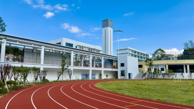 A modern sports facility with a red running track and towers on a sunny day.