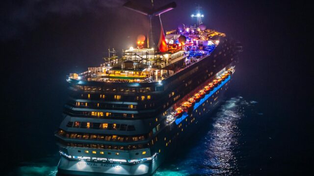 Stunning aerial view of a colorful, illuminated cruise ship navigating the ocean at night.