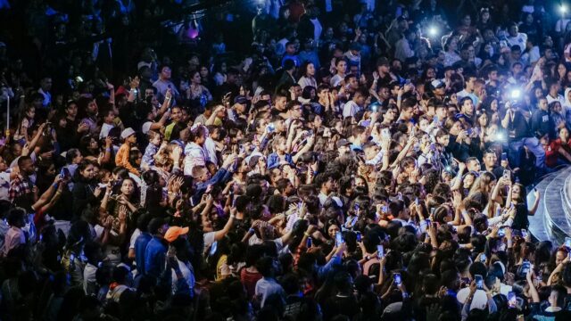 A vibrant crowd enjoying a live concert with phones raised to capture the performance.