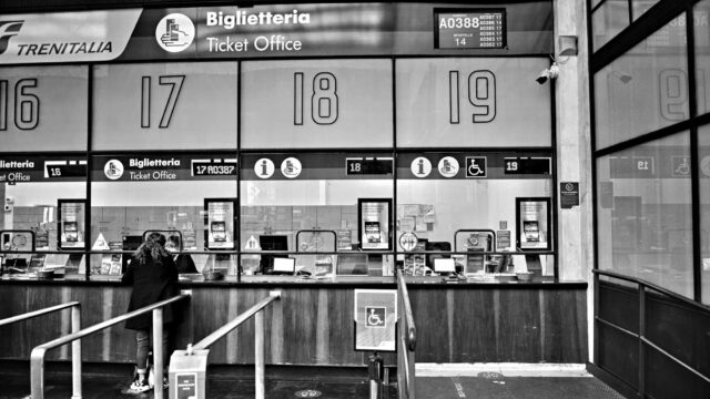 Monochrome image of a train station ticket office with numbered counters, showcasing travel services.