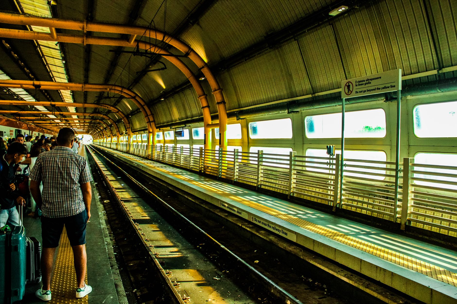 Commuters waiting at a busy urban train station platform with railway tracks.