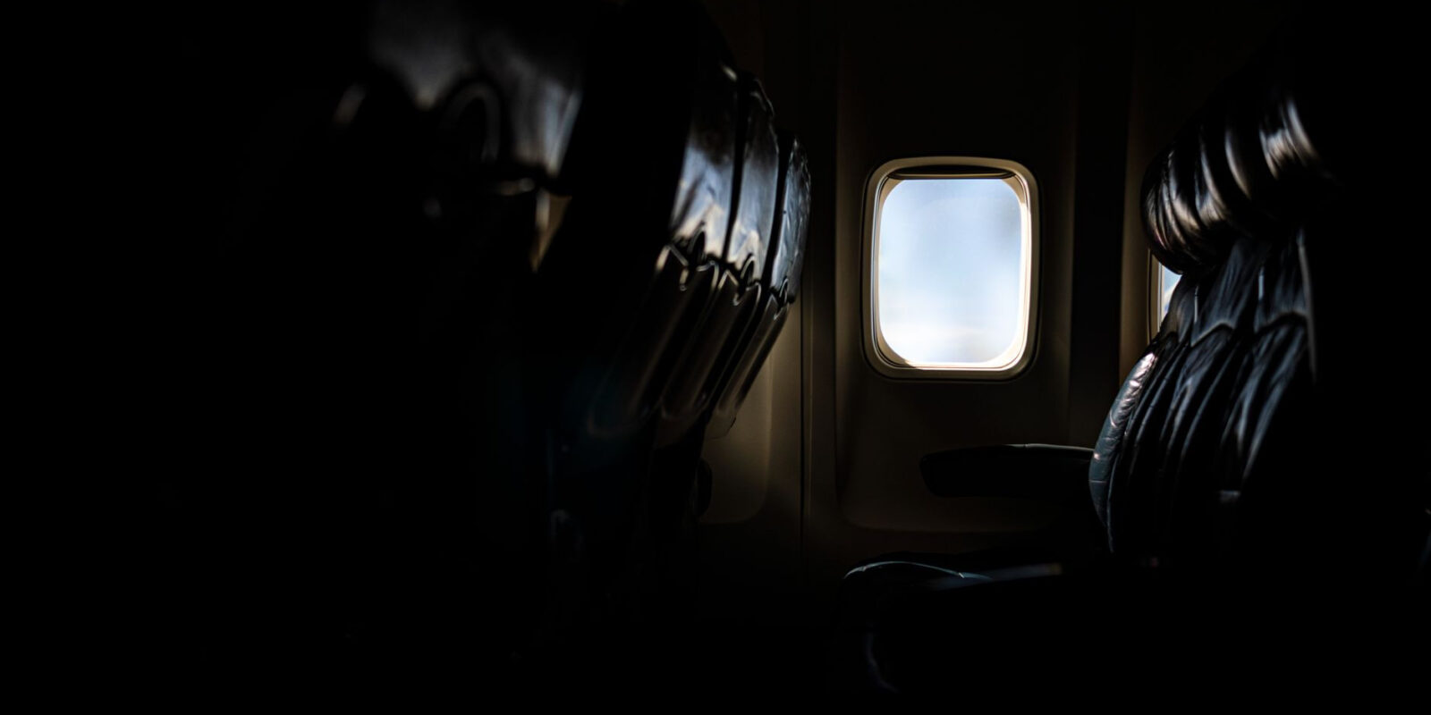 Dark airplane cabin with an illuminated window view during flight.
