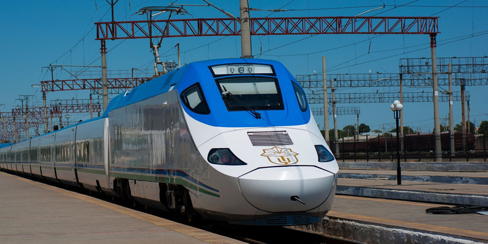High-speed train stationed on tracks under clear blue sky.