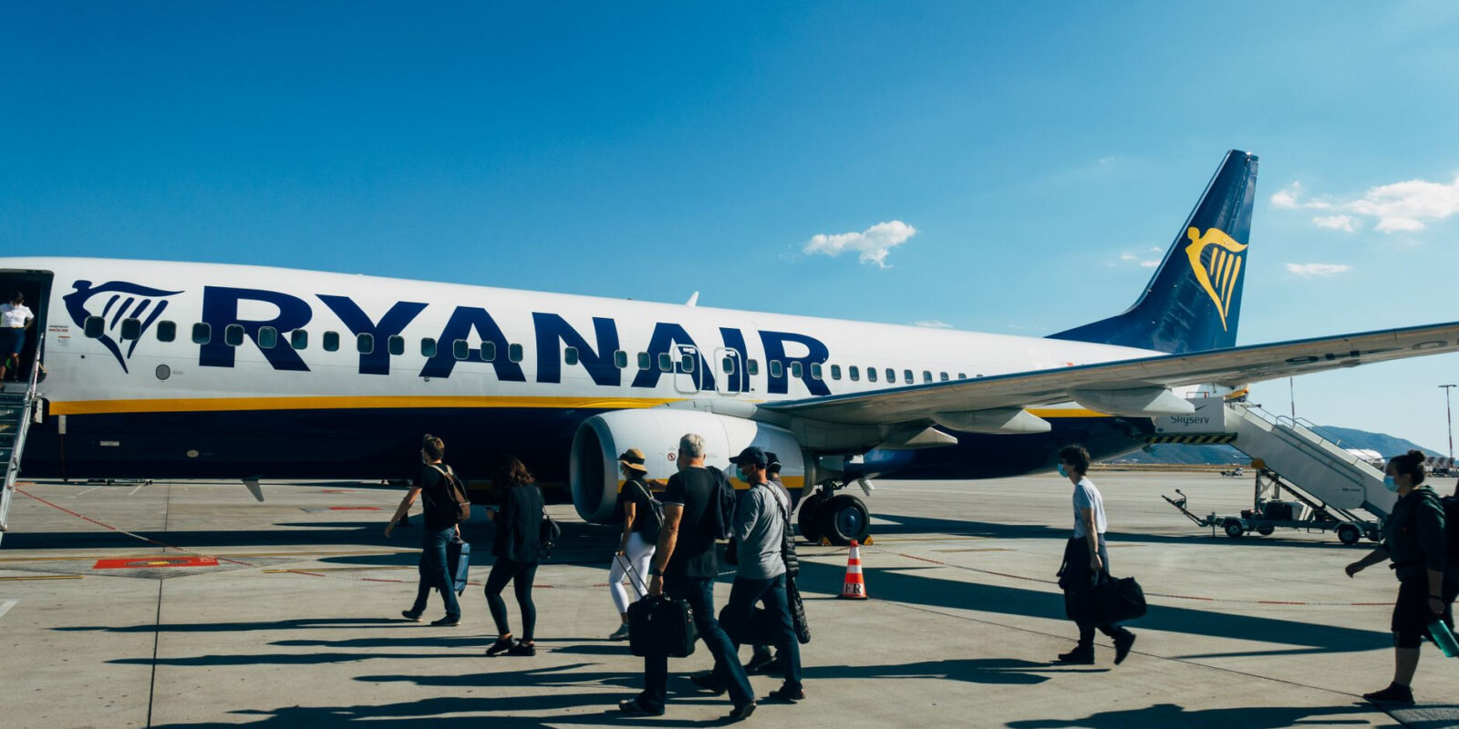 Travelers boarding a Ryanair airplane under clear blue sky at the airport.